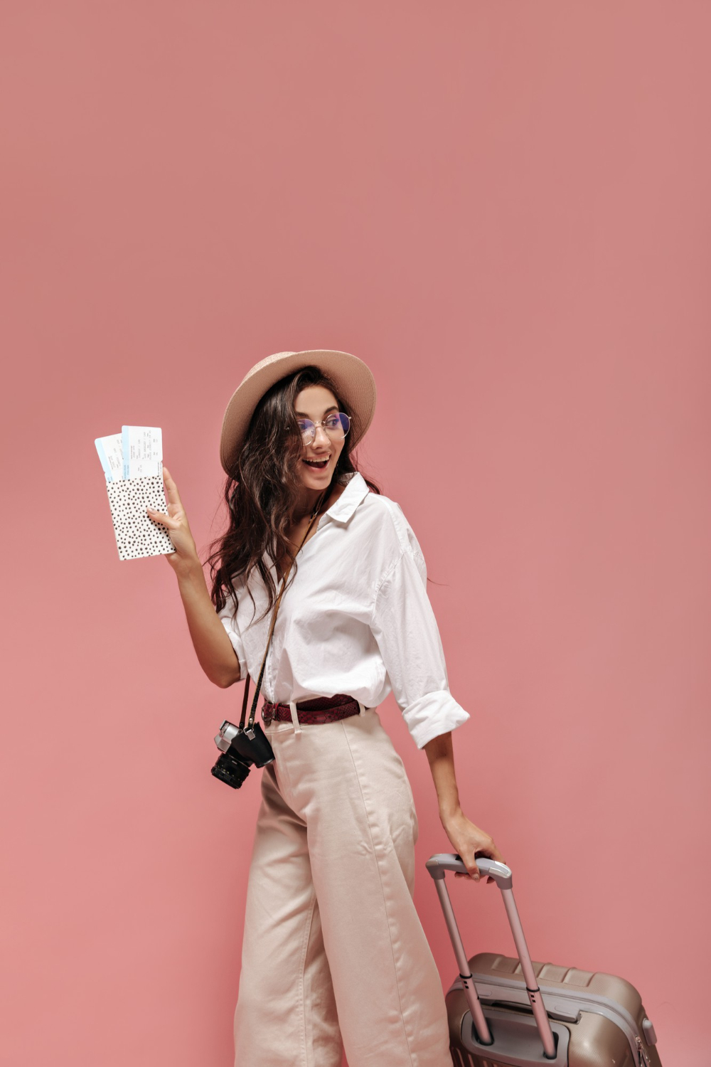 curly-cute-lady-with-brunette-hair-white-wide-sleeve-shirt-beige-pants-modern-belt-stylish-eyeglasses-posing-with-plane-tickets